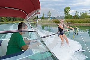 Woman water skiing holding bar protruding from boat