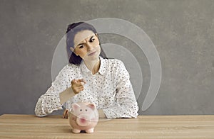 Woman waves a punishing finger at the piggy bank as a sign that she will now be more frugal.