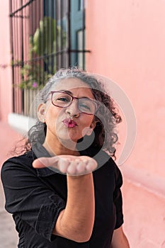 Woman with wavy hair blowing a kiss in the street