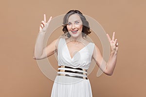 Woman with wavy hair shows peace v sign, smiles toothily enjoys nice day, gestures victory symbol.