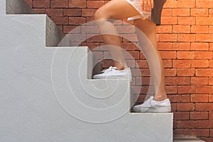 Woman wear black t-shirt and white shorts , her is walking up concrete stairs outside the buildings with red brick wall background