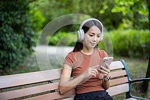 Woman wear headphone and use mobile phone at park
