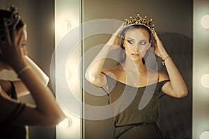 Woman wear jewelry crown at mirror. Beauty queen with glamour look in dressing room. Girl princess and reflection in