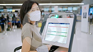 Woman wear mask using self service check-in kiosk at the international airport terminal. Touchscreen and see information on screen