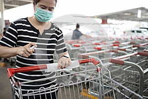 Woman wear mask,using spraying alcohol antiseptic,disinfecting spray,cleaning on shopping cart,trolley handle,protection during photo
