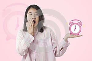 Woman wear pink pajamas yawn and holding alarm clock  feeling sleepy