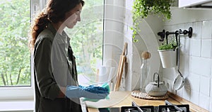 Woman wear protective gloves cleans countertop table standing in kitchen