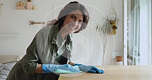 Woman wear protective gloves cleans table smiles looking at camera