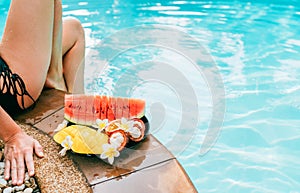 Woman weared swimsuit sitting on swimming pool side with plate of tropical fruits photo