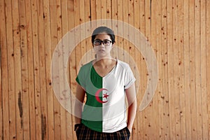 Woman wearing Algeria flag color shirt and standing with two hands in pant pockets on the wooden wall background