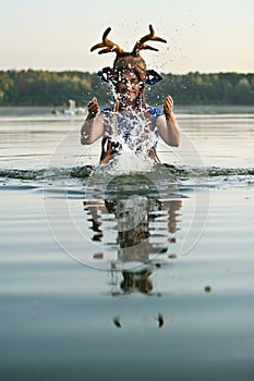 Una mujer agotador cornamenta ciervo un sombrero a azul ropa es un permanecer en ascendiendo su manos arriba salpicar Agua 