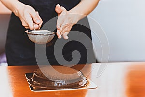 Woman wearing apron powdering chocolate cake with cocoa powder.