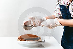 Woman wearing apron powdering chocolate cake with cocoa powder.