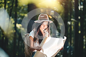 Woman wearing backpack and hat hold in hands location map