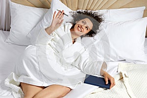 Woman Lying in big white Bed With Pen And Notepad