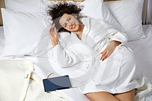 Young curly Woman Lying in big white Bed With Pen And Notepad