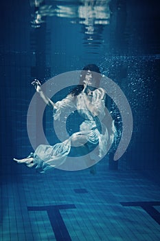 Woman wearing beautiful dress underwater in a swimming pool