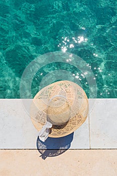 Woman wearing big summer sun hat relaxing on pier by clear turquoise sea.