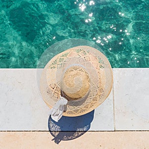 Woman wearing big summer sun hat relaxing on pier by clear turquoise sea.