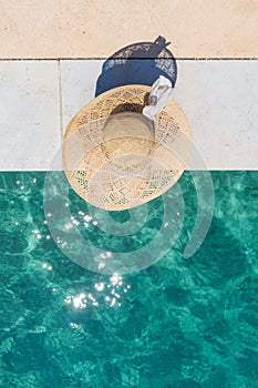 Woman wearing big summer sun hat relaxing on pier by clear turquoise sea.