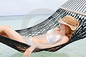 Woman Wearing Bikini And Sun Hat Relaxing In Beach Hammock