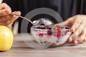 Woman wearing black shirt eats a fresh homemade glass bowl of creamy yogurt parfait