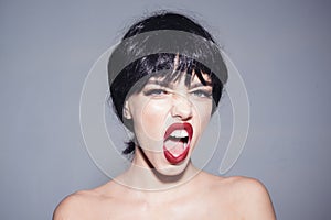 Woman wearing black wig on gray background. Girl with red lips makeup shouting, madness concept