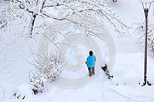 Woman wearing a blue coat and black weal stands in a park covered with snow in winter. View from above photo