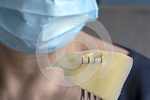 Woman wearing blue medicine mask holds fork with cheese slice. Selective focus