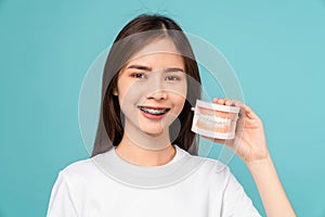 woman wearing braces holding tooth model on blue background, Concept oral hygiene and health care