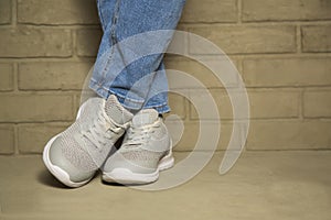 Woman wearing casual clothing and white sneakers leaning wall in city.