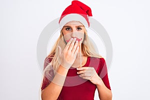 Woman wearing Christmas Santa hat holding fanny mustache over isolated white background cover mouth with hand shocked with shame