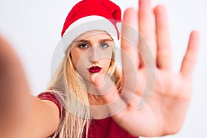 Woman wearing Christmas Santa hat make selfie by camera over isolated white background with open hand doing stop sign with serious