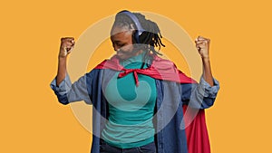 Woman wearing cloak posing as hero in costume kissing biceps, studio background