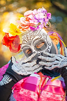 Woman wearing colorful skull mask and paper flowers for Dia de Los Muertos/Day of the Dead