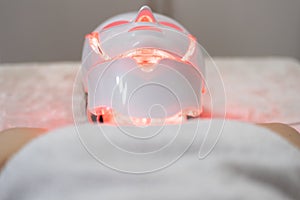 Woman is wearing cosmetic face photon mask. Health and beauty. Cosmetic procedure for woman face. Beauty laboratory. LED Facial