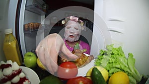 A woman wearing a cosmetic mask looks in the refrigerator for food.
