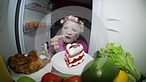 A woman wearing a cosmetic mask looks in the refrigerator for food.
