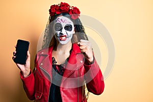 Woman wearing day of the dead costume holding smartphone showing screen annoyed and frustrated shouting with anger, yelling crazy