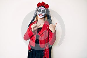 Woman wearing day of the dead costume over white pointing to the back behind with hand and thumbs up, smiling confident