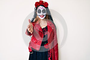 Woman wearing day of the dead costume over white smiling friendly offering handshake as greeting and welcoming