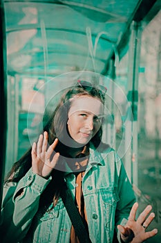 A woman wearing a denim jacket is standing at a bus stop, touching the glass with her hands. Public transportation, urban life,