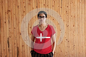 Woman wearing Denmark flag color shirt and standing with two hands in pant pockets on the wooden wall background