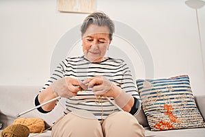 Woman wearing domestic clothes holding knitting needles while knitting