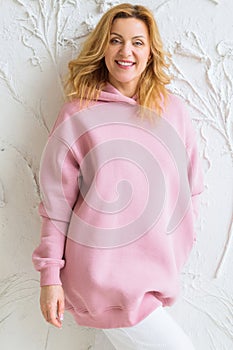 Woman wearing empty pink hoodie and posing against a white wall