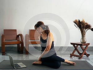 Woman wearing exercise suit ,sitting on yoga mat,crossed legs and twist body to left side