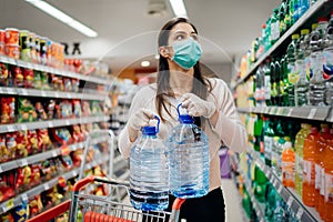 Woman wearing face mask buying bottled water in supermarket/drugstore with sold-out supplies.Prepper buying bulk supplies