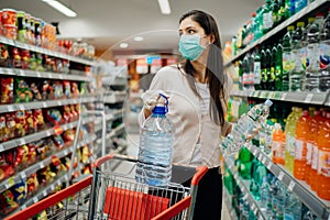 Woman wearing face mask buying bottled water in supermarket/drugstore with sold-out supplies.Prepper buying bulk supplies due to