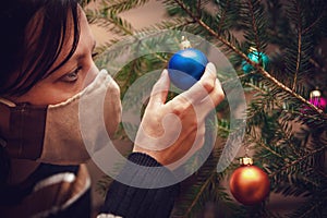 Woman wearing a face mask and is decoration a christmas tree with baubles or balls