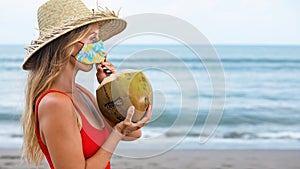 Woman wearing face mask drinking young coconut on tropical beach